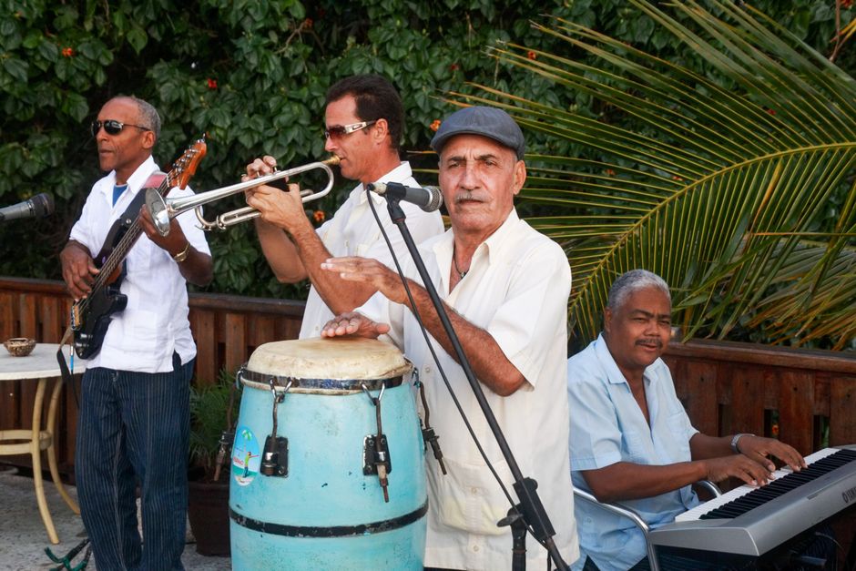 Group of musicians performing outdoors, featuring guitar, trumpet, conga, and keyboard, showcasing live music and teamwork.
